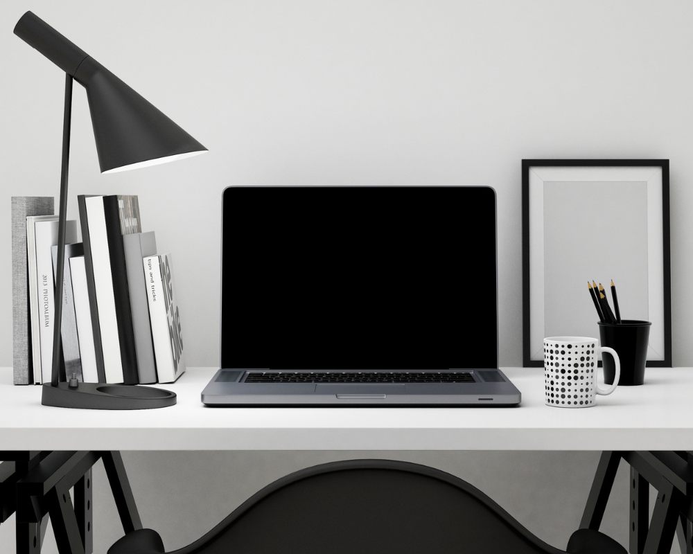 Minimal black and white desk with a laptop, lamp and design books